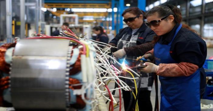 Women wearing sunglasses work at a production line manufacturing electric machine parts at a