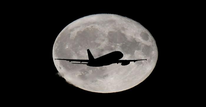 A passenger plane passes in front of the full moon as it makes it's final landing approach to