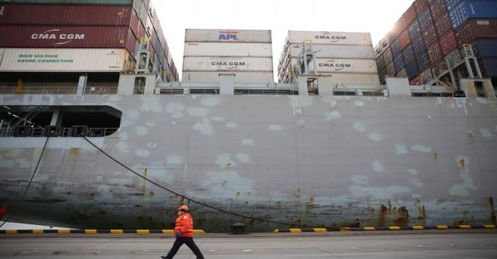 Worker wearing a face mask walks past a cargo ship at a container terminal of Qingdao port