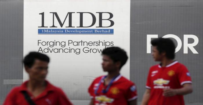 Men walk past a 1 Malaysia Development Berhad (1MDB) billboard at the fund's flagship Tun Razak