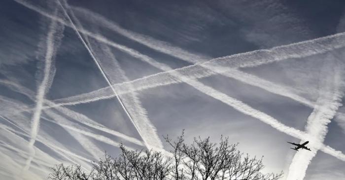 A passenger plane flies through aircraft contrails in the skies near Heathrow Airport in west