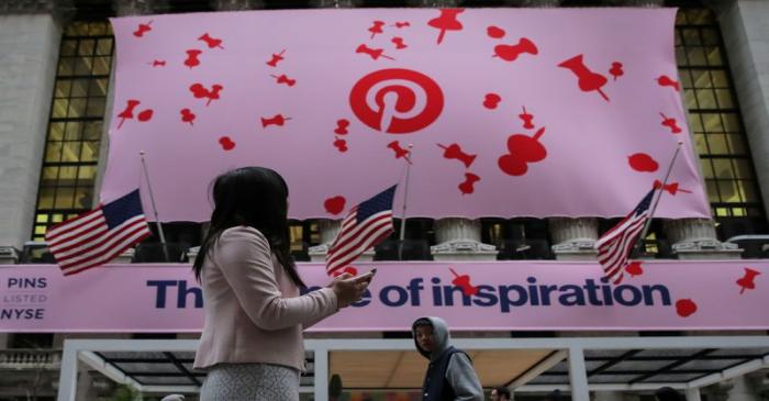 A woman uses her phone as a banner celebrating the IPO of Pinterest Inc. hangs on the front of