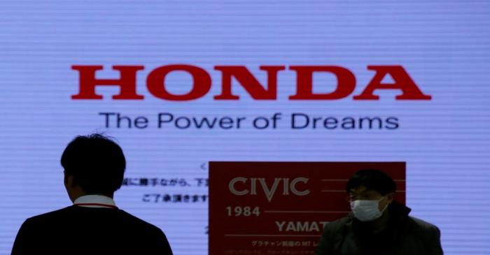 Men are silhouetted against a logo of Honda Motor at the company's showroom in Tokyo