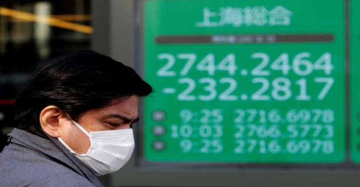 FILE PHOTO:  A man wearing a surgical mask stands in front of a screen showing Shanghai