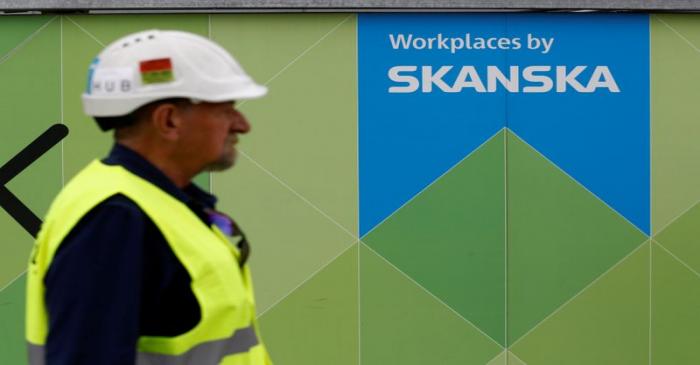 FILE PHOTO: A worker walks past a Skanska logo seen on a fence at a construction site In