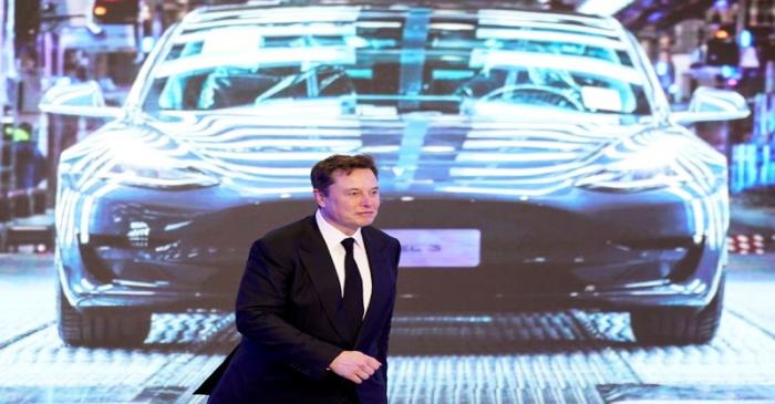 Tesla Inc CEO Elon Musk walks next to a screen showing an image of Tesla Model 3 car during an