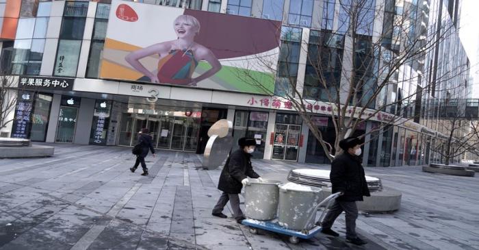 Clean workers move the snow past closed stores at a shopping area in Beijing