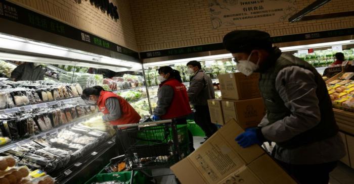 Staff members wearing face masks place vegetables onto shelves at a JD.com's 7Fresh chain