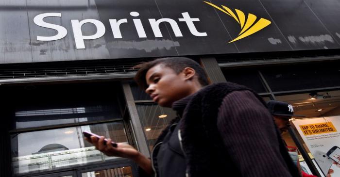 FILE PHOTO: A woman uses her phone as she walks past a Sprint store in New York's financial