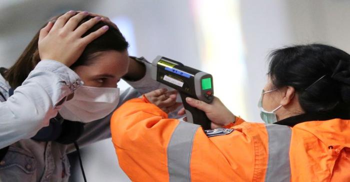 FILE PHOTO: A worker checks the temperature of a passenger arriving into Hong Kong