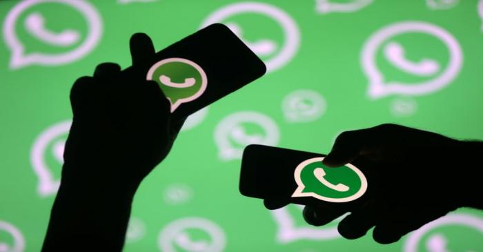 Men pose with smartphones in front of displayed Whatsapp logo in this illustration