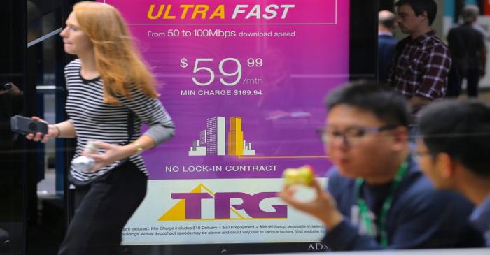 A woman looks at her phone as she walks past an advertisement for Australia's TPG Telecom Ltd