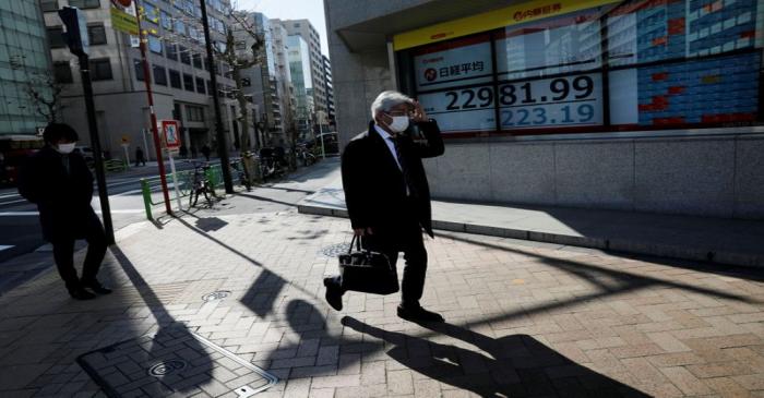 FILE PHOTO: People wearing surgical masks walk past a screen showing Nikkei index outside a