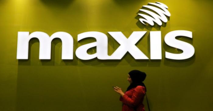 FILE PHOTO: A woman walks past a logo of Maxis at its headquarters in Kuala Lumpur