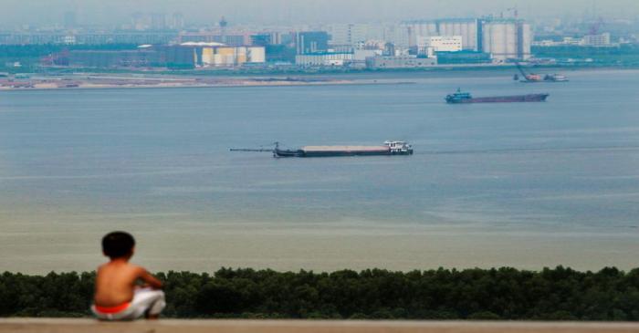 FILE PHOTO: Boy looks at cargo ships passing along the Pearl River in Guangzhou, Guangdong