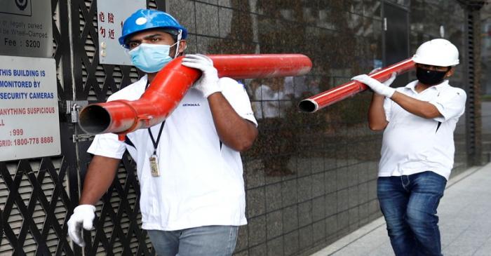 Construction workers wearing masks in precaution of the coronavirus outbreak carry pipes as