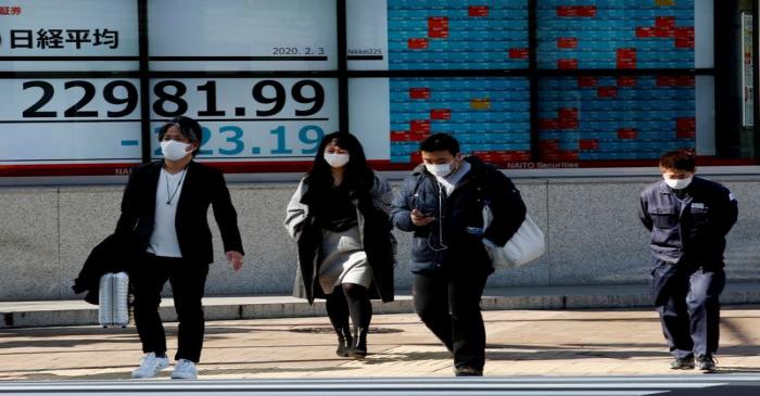 People wearing surgical masks walk past a screen showing Nikkei index outside a brokerage in