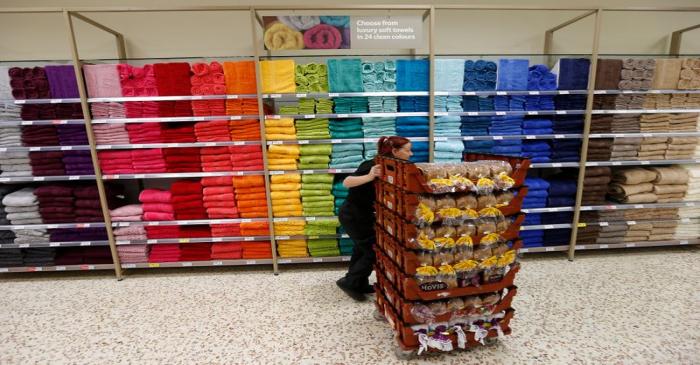 A bakery employee pushes a cart with loaves of bread past a towel display at a Tesco Extra