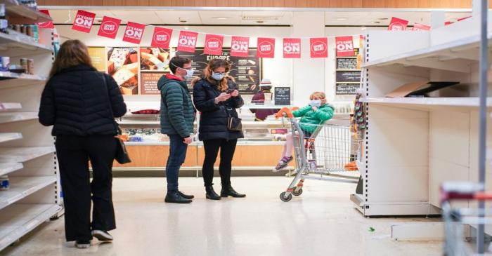 FILE PHOTO: People wearing protective face masks stand next to empty shelves in a supermarket,