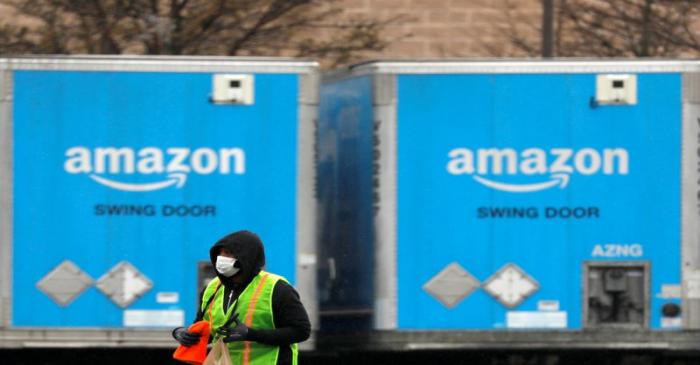 A worker in a face mask walks by trucks parked at an Amazon facility as the global coronavirus