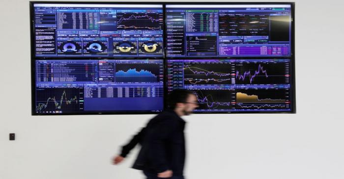 FILE PHOTO: A man walks past screens displaying market data at CMC Markets in London