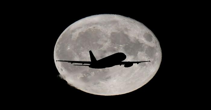 FILE PHOTO: A passenger plane passes in front of the full moon as it makes it's final landing