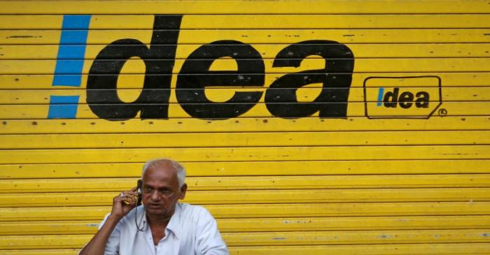 FILE PHOTO: A man speaks on his mobile phone as he sits in front of a shop displaying the Idea