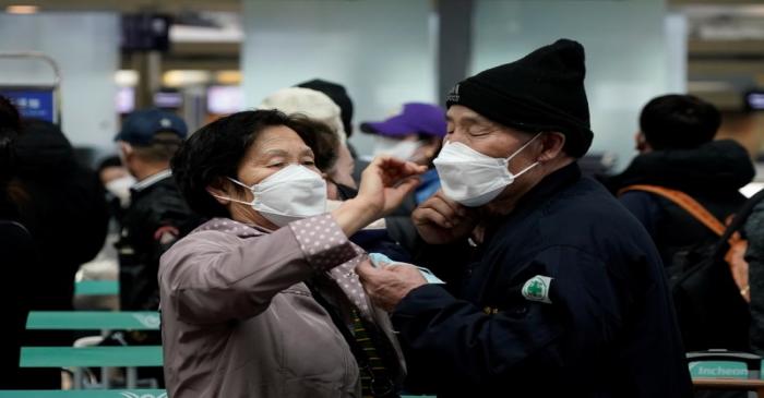 A woman wearing a mask to prevent contracting the coronavirus adjusts her husband's mask as