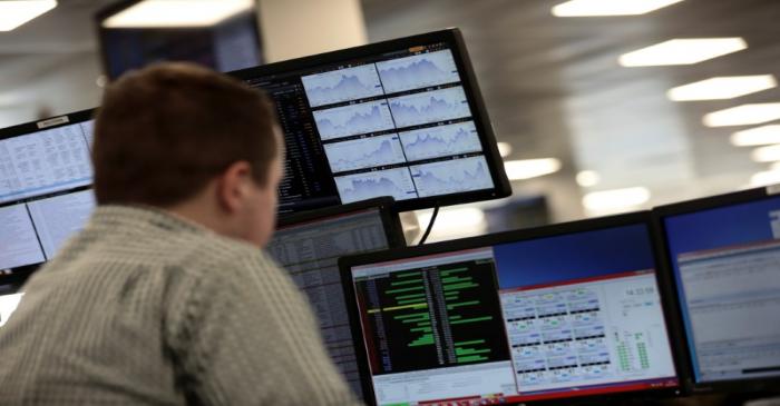 FILE PHOTO: Traders looks at financial information on computer screens on the IG Index trading