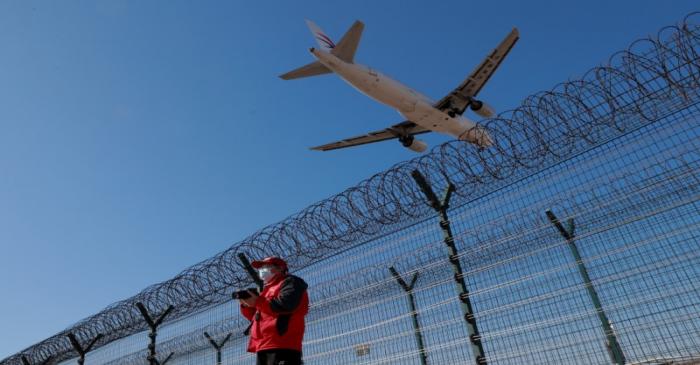 A man wearing a protective mask stands at a fence surrounding Beijing Capital International as