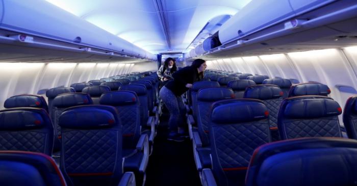 Air travelers grab carry-on luggage behind rows of empty seats aboard a Delta flight from New