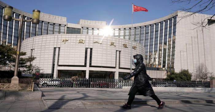 FILE PHOTO: Man wearing a mask walks past the headquarters of the People's Bank of China, the