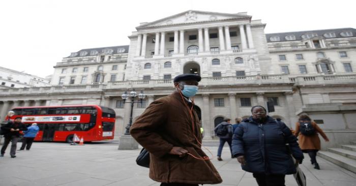 FILE PHOTO: A man, wearing a protective face mask, walks in front of the Bank of England,