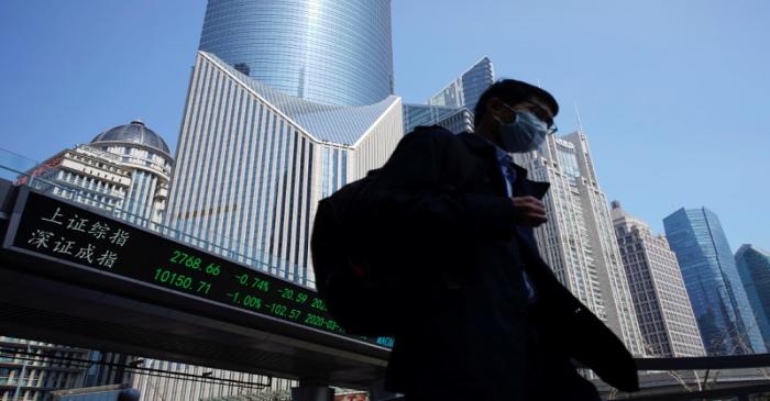 Pedestrian wearing a face mask walks near an overpass with an electronic board showing stock
