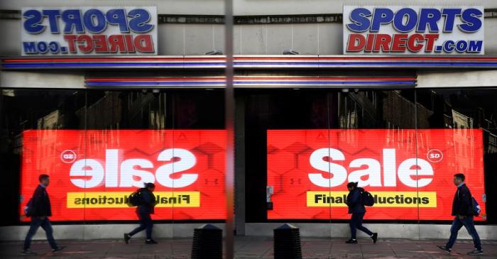Pedestrians are seen reflected in a window as they pass a branch of Sports Direct on Oxford