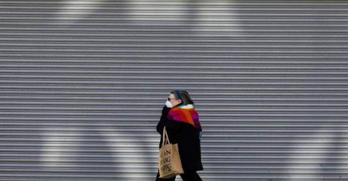 A woman walks past a shuttered shop in London