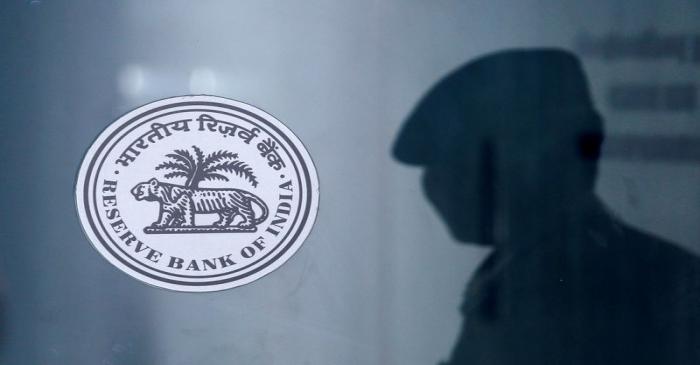 A security guard's reflection is seen next to the logo of the Reserve Bank Of India (RBI) at