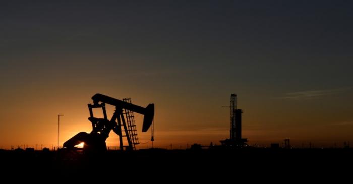 FILE PHOTO: A pump jack operates in front of a drilling rig at sunset in an oil field in Texas