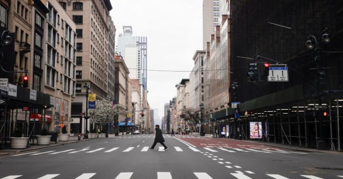 A man crosses a nearly empty 5th Avenue in midtown Manhattan during the outbreak of the
