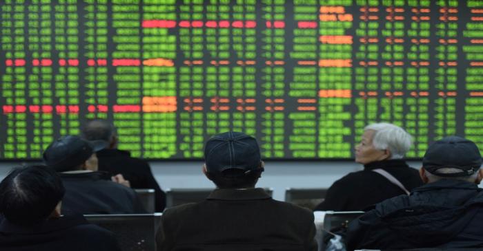 Investors sit in front of a board showing stock information at a brokerage house on the first