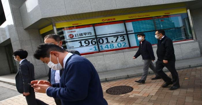 People wearing protective face masks are seen near an electronic display showing the Nikkei