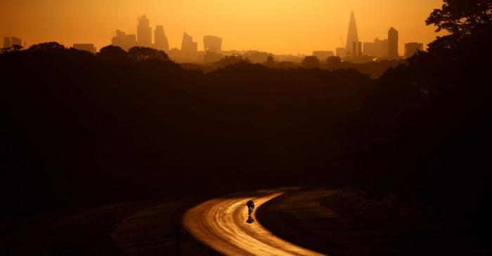 FILE PHOTO: The sun rises behind The Shard and the financial district as a cyclist rides