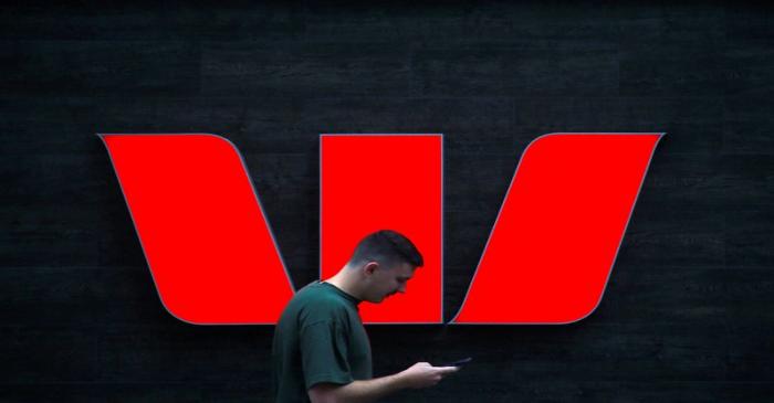 A pedestrian looks at his phone as he walks past a logo for Australia's Westpac Banking Corp