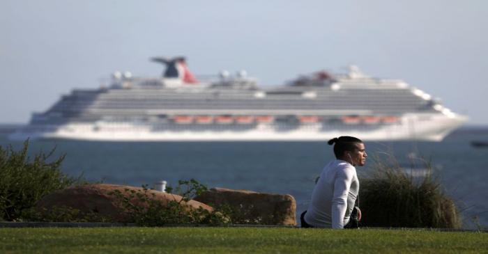 A person stretches at a park overlooking the Pacific Ocean and Carnival Panorama cruise ship as