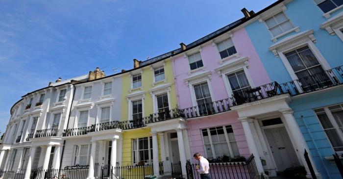 A man walks past houses painted in various colours in a residential street in London