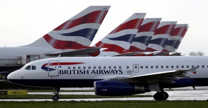 FILE PHOTO: BA plane taxis past tail fins of parked aircraft to runway near Terminal 5 at