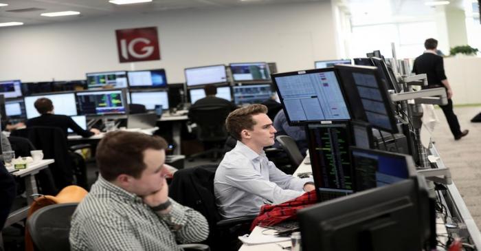 FILE PHOTO: Traders look at financial information on computer screens on the IG Index trading