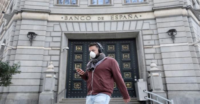 FILE PHOTO: A man wears a protective face mask as he walks past Banco de Espana (Bank of