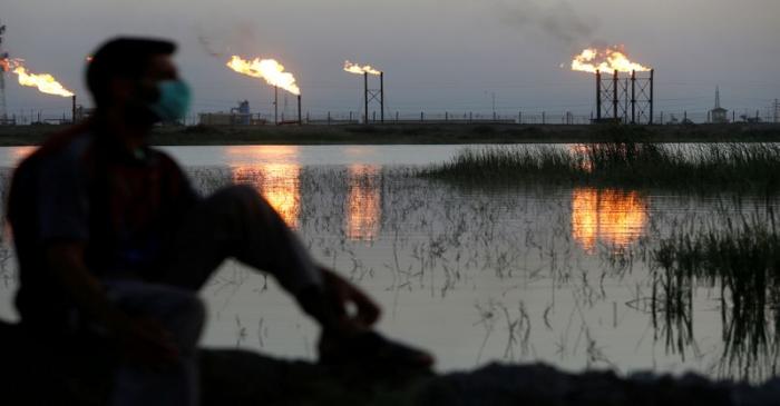 FILE PHOTO: Flames emerge from flare stacks at Nahr Bin Umar oil field, as a man is seen