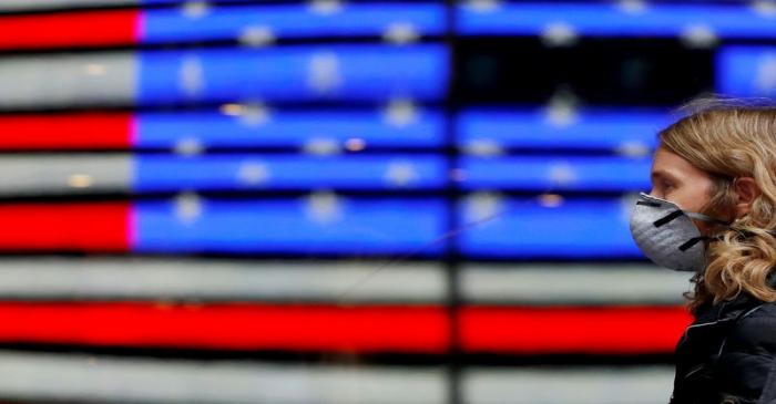 A person in a surgical mask walks by a reflection of the flag of the United States as the